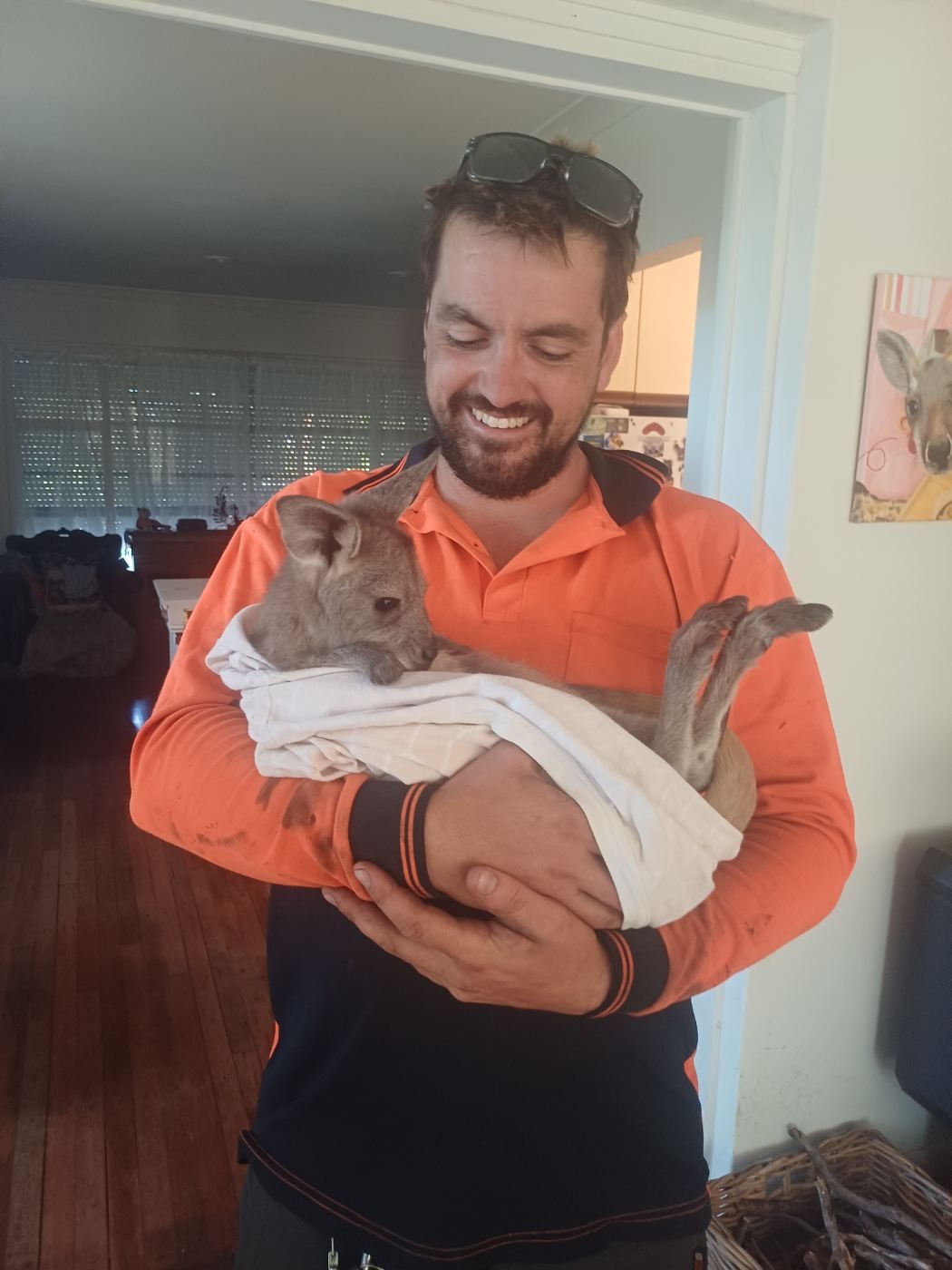 Bushmasters crew member in hi-vis holding a joey wrapped in a towel