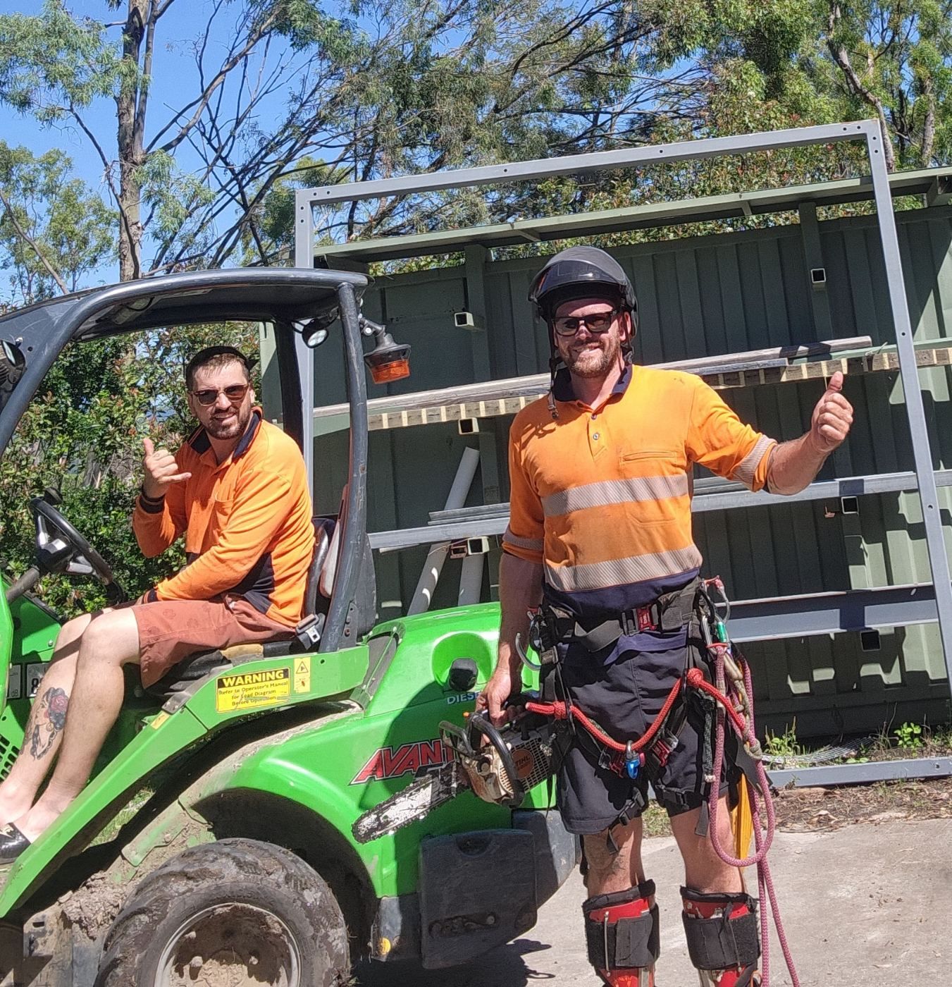 Jordan and Luke of Bushmasters Tree Services in hi-vis, one in a compact loader and one in climbing gear
